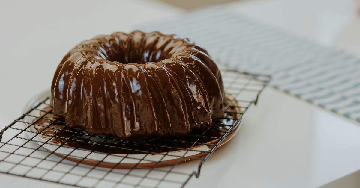 A glazed chocolate looking bunt cake cooks on a rack